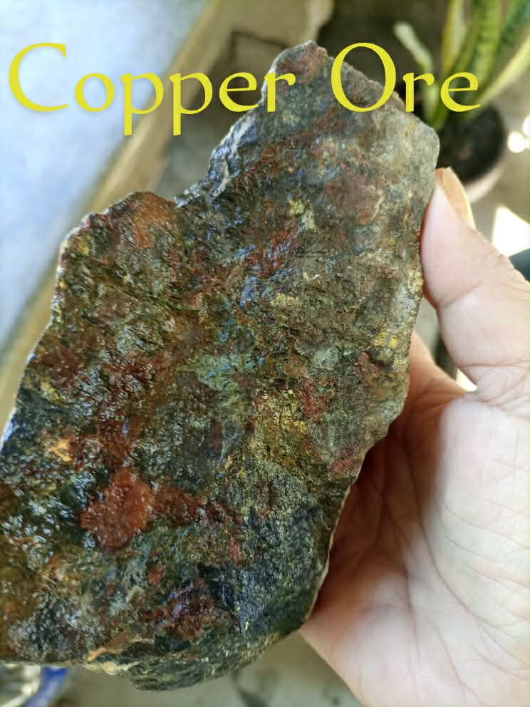 A labeled mineral-bearing rock held in a person's hand